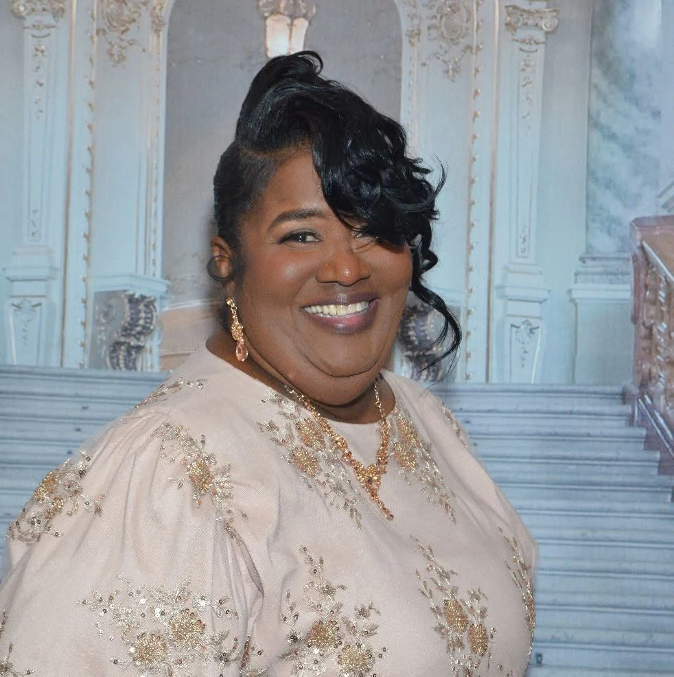 Overseer Turlyn Betterson smiling in a cream dress with gold embroidery