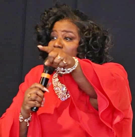 Overseer Betterson preaching with a microphone, in red