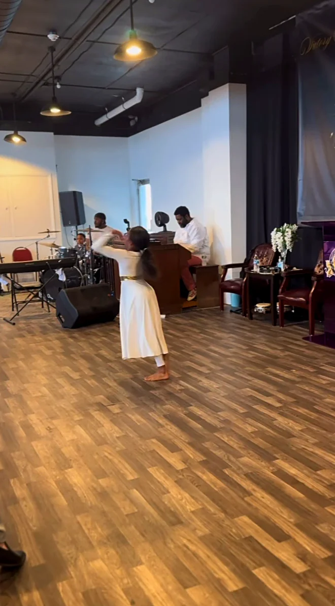 A girl in a white dress praise-dances across the floor of the sanctuary