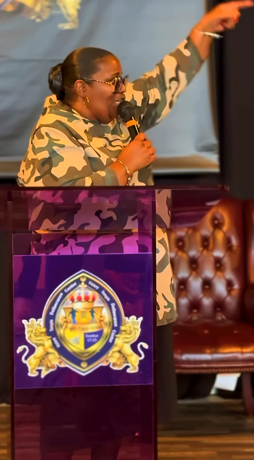 A minister points heavenward while preaching from the purple VTDC pulpit with the gold crest
