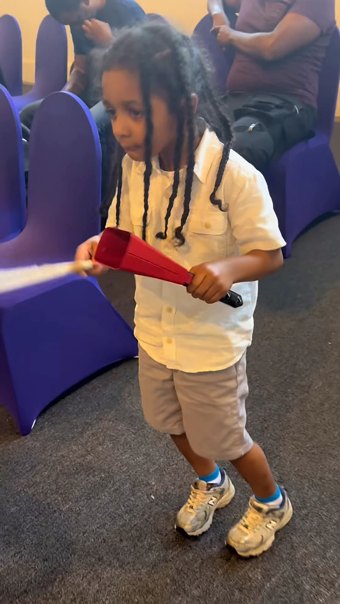 A young boy keeps time on a red cowbell in the aisle