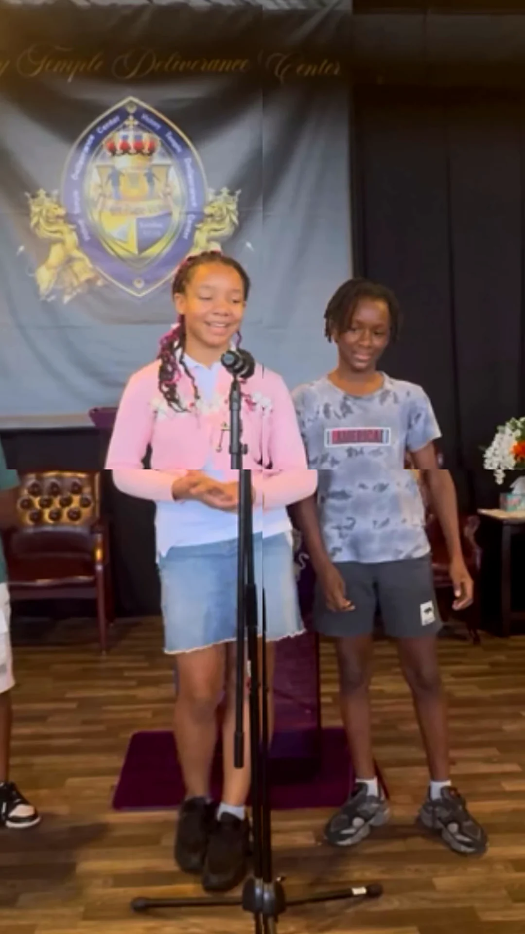 Two young people sing at the microphone in front of the VTDC crest banner